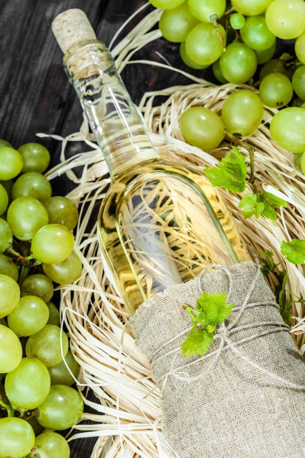 A bottle of white wine with white grapes in a wooden background.